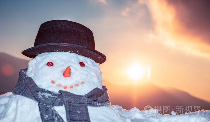 傍晚时分，在日落的天空背景下，一个微笑的雪人在户外的肖像，良好的冬季传统，快乐的寒假概念