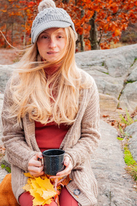 女人在户外手里拿着一杯茶。 美丽的女人在秋天的森林里喝热茶。