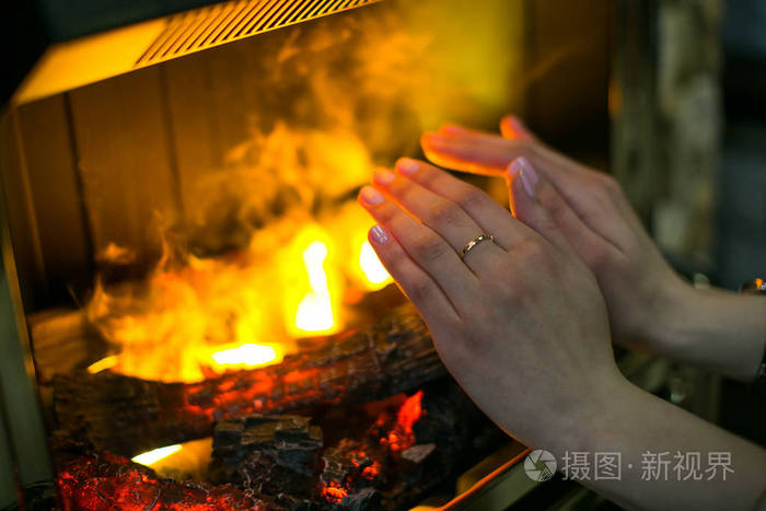 一个年轻的女孩正在空壁炉前暖和她的手双手合拢