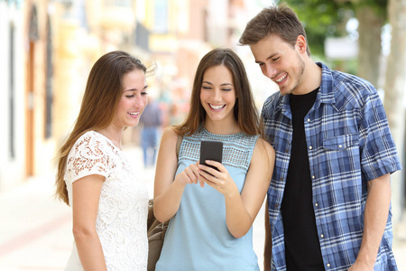 三个快乐的朋友站在街上检查智能手机的内容