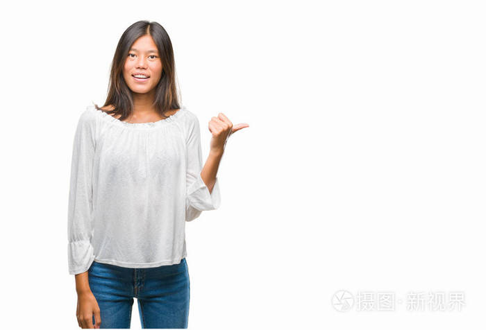 年轻的亚洲女人在孤立的背景上微笑，快乐的脸，看着，用拇指指向一边。
