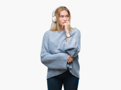 年轻的高加索女人听音乐，戴着耳机，在孤立的背景上看，压力和紧张，双手咬着嘴的指甲。 焦虑问题。