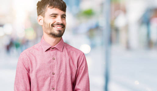 年轻英俊的男人穿着粉红色的衬衫，在孤立的背景上看着一边，脸上带着微笑，自然的表情。 自信地笑着。