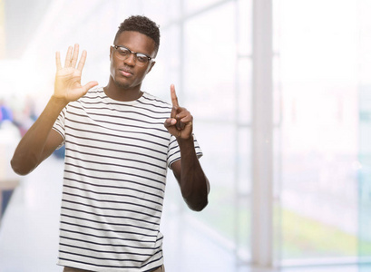 年轻的非洲裔美国男子戴着眼镜和海军t恤，用6号手指举着，微笑着自信和快乐。