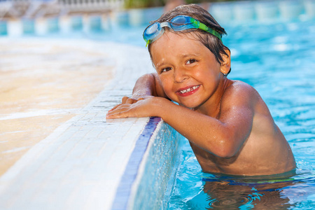 7岁男孩戴着护目镜站在游泳池边上的水中