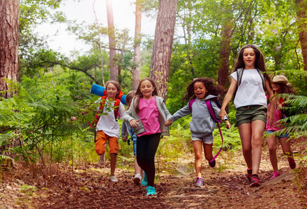 在学校的自然露营旅行中，男孩和女孩一起在森林里奔跑，手牵手在小径上行走
