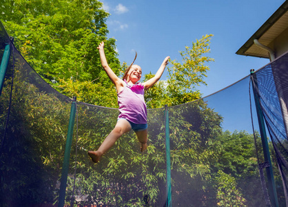 夏天,青春期少女在户外蹦床上蹦蹦跳跳的低角度肖像画照片