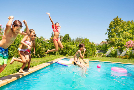 一群快乐的朋友，十几岁的男孩和女孩在夏天在户外游泳池里跳跃。