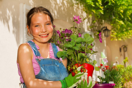 特写一幅美丽的青春期前女孩的肖像，站在阳台花园里，拿着盆栽草莓植物