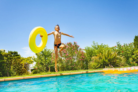 阳光明媚的一天，十几岁的男孩在室外游泳池里跳着一个大游泳圈。
