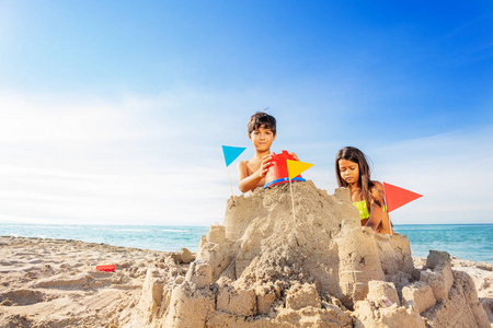 快乐的男孩和女孩在海边用玩具桶建造大沙堡