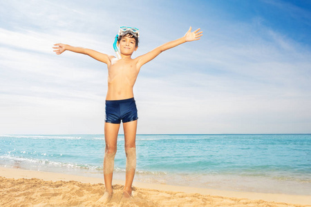 夏天，穿着水肺面罩站在海滩上，双手撑着热带海景的少年儿童的全长画像