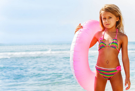 美丽的比基尼女郎在海滩上摆着粉红色的游泳圈的肖像。