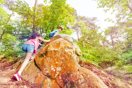 阳光明媚的夏天，两个小孩子在森林里的岩石上爬山和玩耍