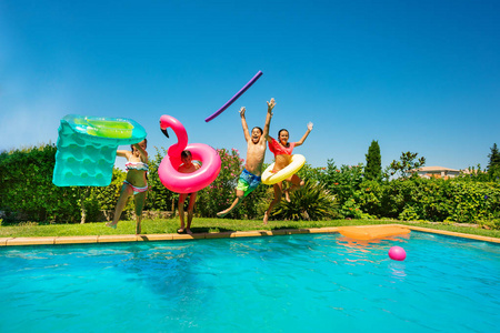 四个十几岁的男孩和女孩带着游泳工具跳进水里度过暑假在游泳池旁。