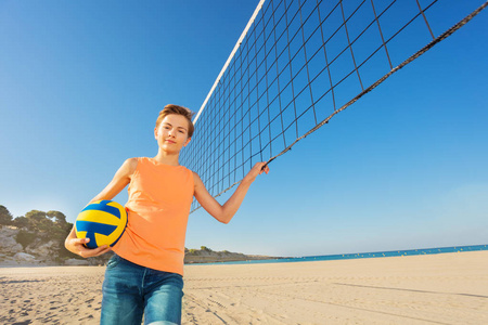 青少年男孩站在网旁，用球准备沙滩排球比赛