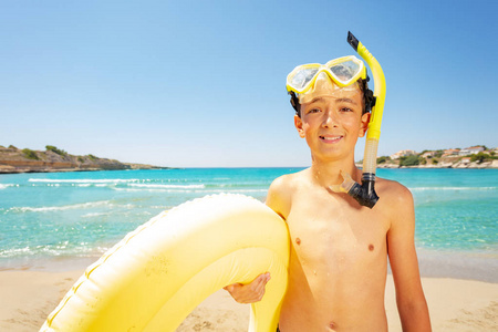 戴着水肺面具站在海滩上，戴着黄色游泳圈的十几岁男孩的肖像。