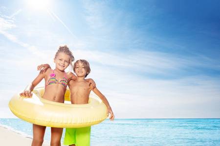 有趣的男孩和女孩站在一起，穿着黄色的大游泳管在海滩上度过夏天的肖像。