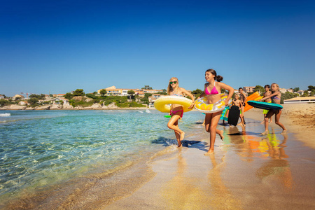 快乐的十几岁的男孩和女孩带着橡皮圈跑进大海，在海滩上度过暑假