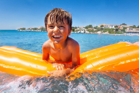 微笑男孩在橙色充气床垫上游泳的肖像，夏天在海边度过