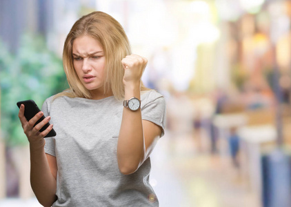 年轻的白种人女人用智能手机在孤立的背景下发送信息，愤怒疯狂和沮丧地大喊大叫，举起手愤怒的概念