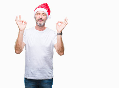 中年老人戴着圣诞帽，在孤立的背景上放松，闭着眼睛微笑，用手指做冥想手势。 瑜伽概念。