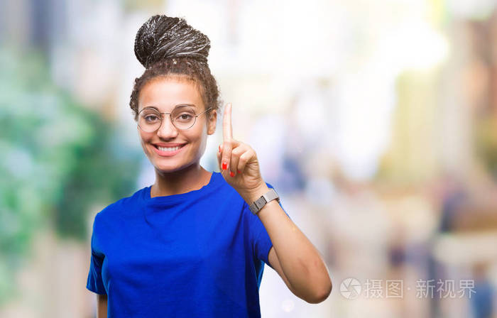 年轻的辫子，非洲裔美国女孩戴着眼镜，在孤立的背景上，用第一根手指，同时微笑，自信和快乐。