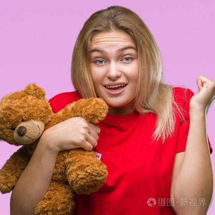 年轻的白种人女人抱着可爱的泰迪熊在孤立的背景下尖叫自豪庆祝胜利和