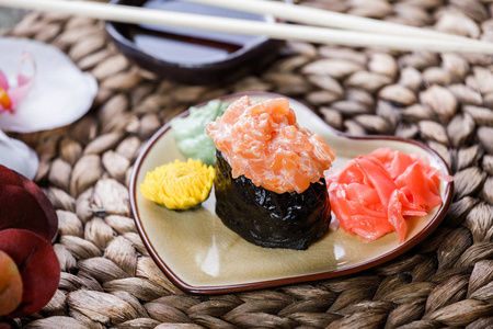 寿司GunkanMaki与鲑鱼在盘子上的竹垫装饰花。 日本料理。 选择性聚焦