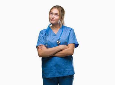 年轻的白种人医生女人穿着外科医生制服，在孤立的背景上微笑着看着一边，凝视着远方的思考。