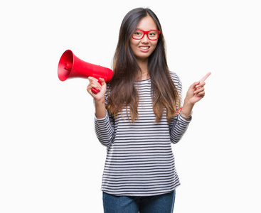 年轻的亚洲女人拿着扩音器在孤立的背景上，非常高兴地用手和手指指向一边