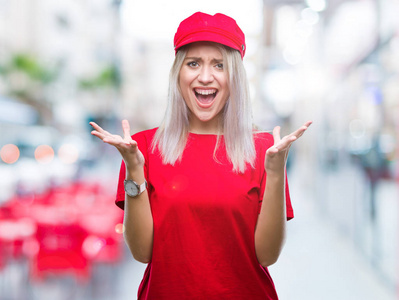 年轻的金发女人戴着红色的帽子，在孤立的背景上庆祝疯狂和疯狂的成功，手臂抬起和闭上的眼睛尖叫兴奋。 赢家概念