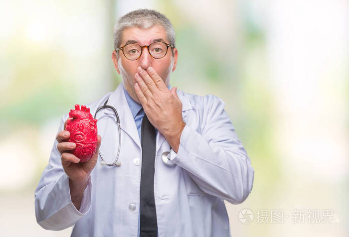英俊的高级心脏病专家医生男子抱着心,用手捂住孤立的背景,捂住嘴