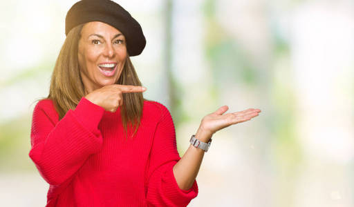 中年成年女性穿着时尚贝雷帽在孤立的背景上惊讶和微笑的相机，同时呈现手和手指。