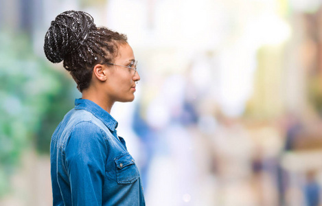 年轻的辫子非裔美国女孩戴着眼镜，在孤立的背景下，看着侧面放松的轮廓，自然的脸，自信的微笑。