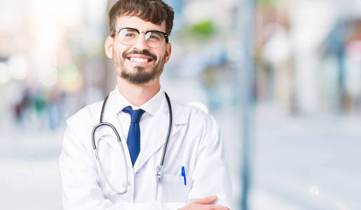 年轻的医生穿着医院的外套，在孤立的背景上，快乐的脸，用交叉的手臂微笑着看着相机。 积极的人。