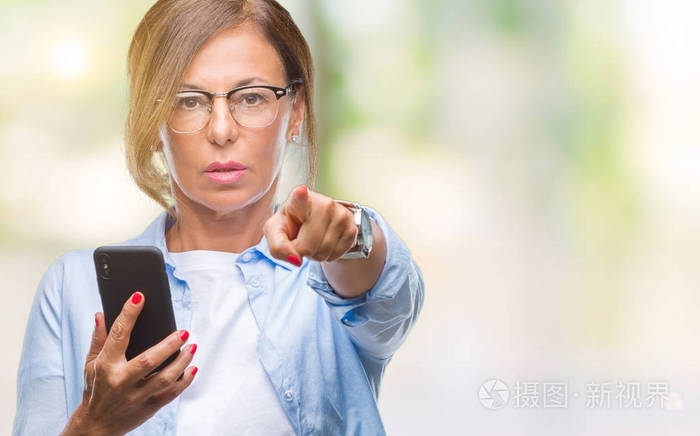 中年妇女用智能手机发短信，在孤立的背景上用手指指向相机，并向你手势正面和自信的手势