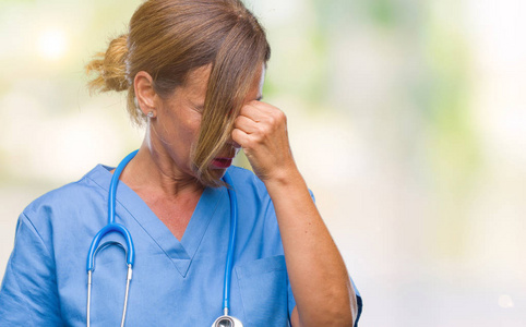 中年高级护士医生女士在孤立的背景下疲惫地揉着鼻子和眼睛,感到疲劳