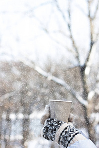 s hands in mittens hold a craft paper glass