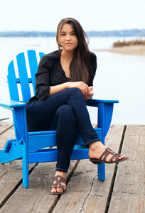 在户外湖边的木墩上坐着蓝色的阿迪朗达克椅子的泰国白种人少女