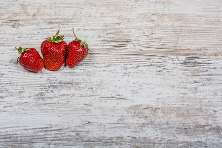 三个草莓在纹理木背景上。 平坦的交叉空间