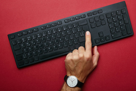 红色背景下黑色电脑键盘上男性手按按钮的俯视图
