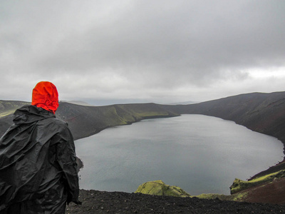 男性冒险家徒步旅行，穿着雨衣，在迷人的自然景观中笑着跋涉，看着火山口湖。 成年男性徒步旅行者返回户外冰岛