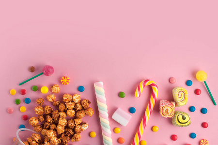 彩色不同的糖果棒棒糖棉花糖焦糖爆米花粉红色背景。 复制空间。 顶部视图