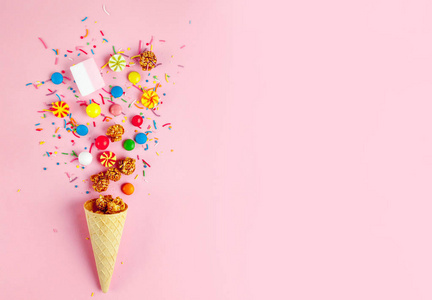 华夫饼角与彩色糖果糖果棉花糖焦糖爆米花甜粉在粉红色背景。 顶级糖果和糖果概念
