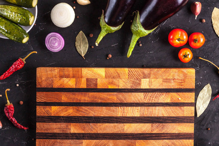茄子，黄瓜，洋葱，西红柿，红色，干辣椒，大蒜湾叶切割板，香料，在黑暗的背景上。 切蔬菜。 顶部视图