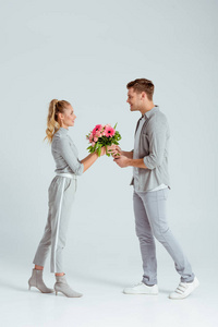 微笑的男人把粉红色的花束送给灰色背景的女人