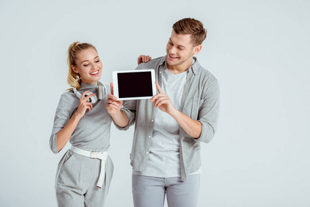 微笑的女人戴着耳机站在男人身边，手里拿着数字平板电脑，灰色的屏幕被隔离开来