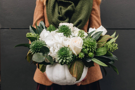 女人手里拿着美丽的花束，上面有白色的花朵和奇异的绿色植物