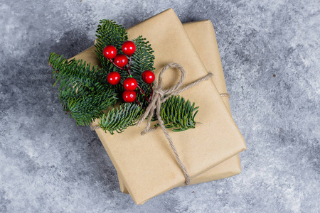 圣诞礼品盒用工艺纸包装，用冷杉树枝和红色浆果装饰在混凝土桌子背景上。 圣诞节礼物和寒假的概念。 平躺着复制空间。